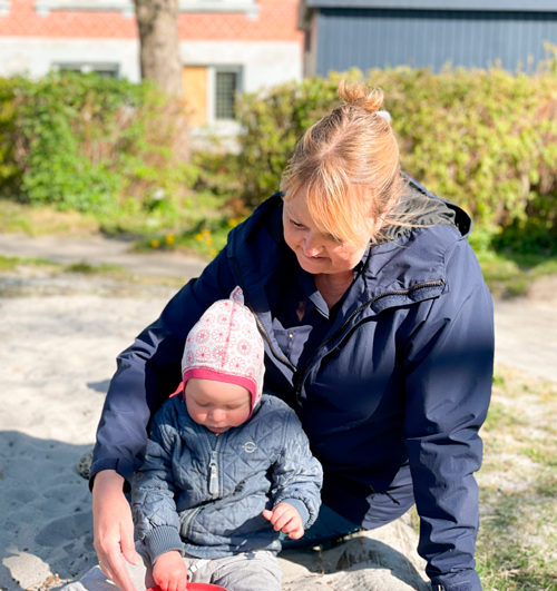 En voksen og et barn sidder ved sandkassen