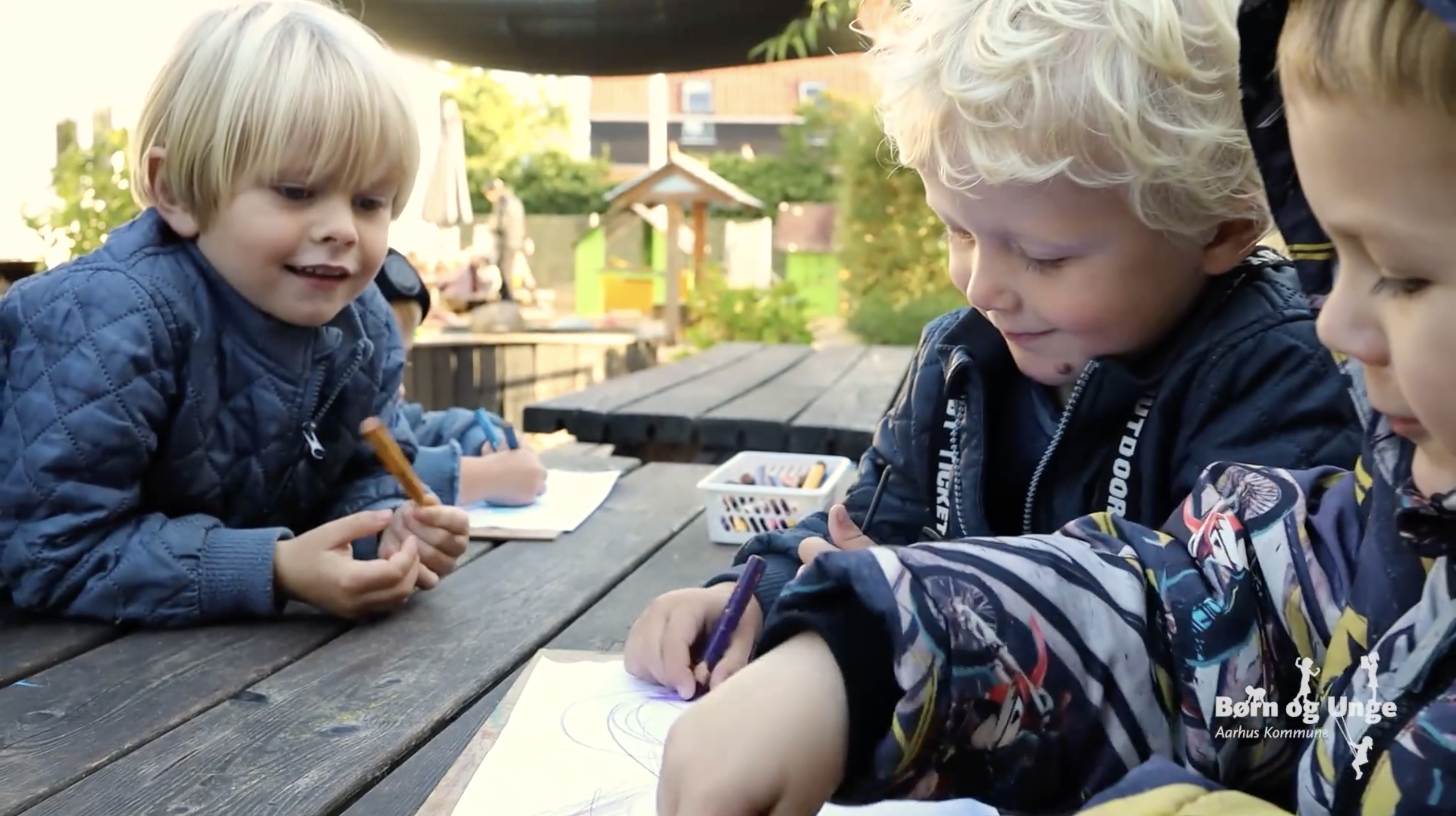 Tre børn tegner ved et bord udenfor